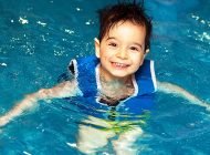 A Kid with blue swimsuit standing and smiling inside the pool