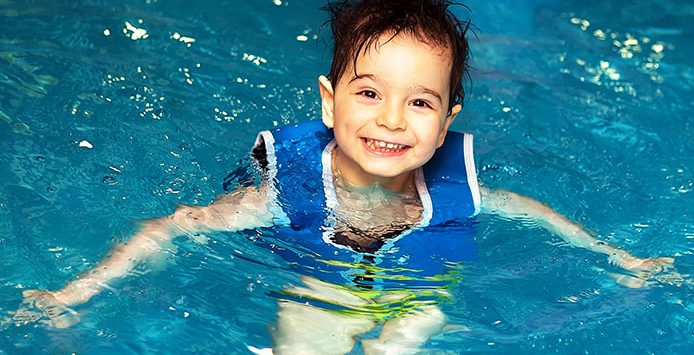 A Kid with blue swimsuit standing and smiling inside the pool