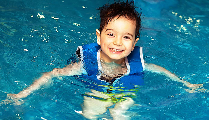 A Kid with blue swimsuit standing and smiling inside the pool